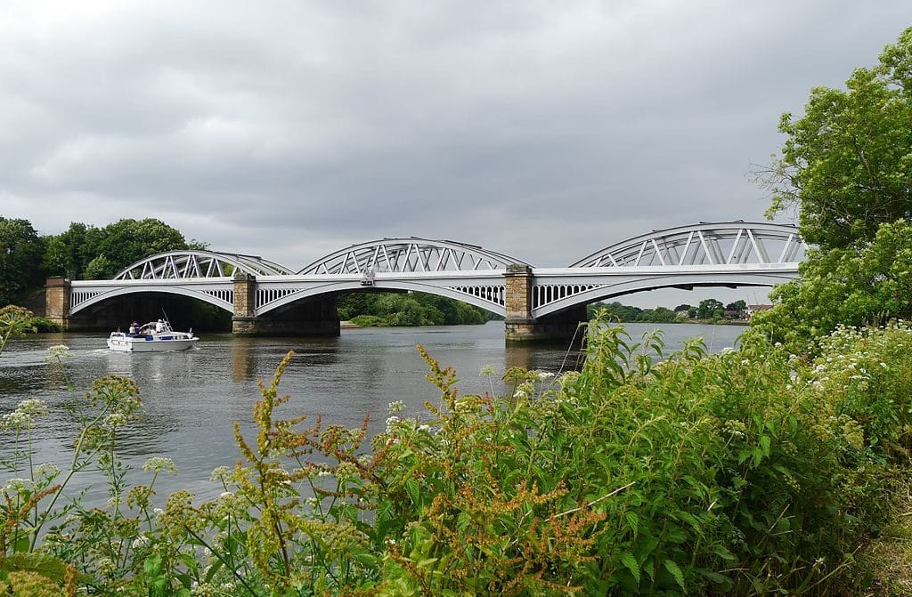 A railway bridge across the river beside leafy residential buildings